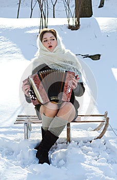 Russian beauty in a white knitted scarf in the snow plays the accordion winter