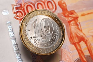 Russian bimetallic 10 ten ruble coin hangs in the air above a 5000 five thousand ruble banknote