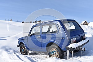 The russian blue colored car model parked in the  deep snow