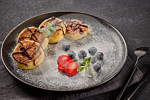 Russian cottage cheese pancakes Syrniki with berries and chocolate sauce on black background