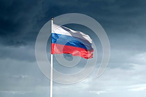 Russian flag on flagpole waving against gloomy rainy clouds on the sky