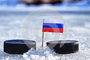 A russian flag on toothpick between two hockey pucks on outdoor ice. A russia playing on World cup in group B. 2019 IIHF Ice