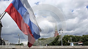 Russian flag waving from wind against red Kremlin wall with towers and green trees in Moscow on sunny day