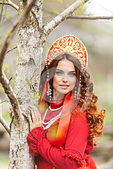 russian girl in traditional russian sarafan and kokoshnik embroidering outdoors