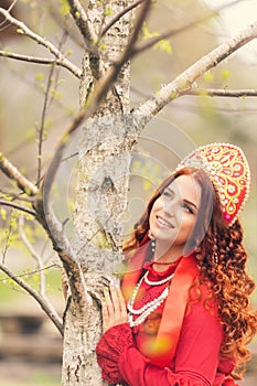 russian girl in traditional russian sarafan and kokoshnik embroidering outdoors