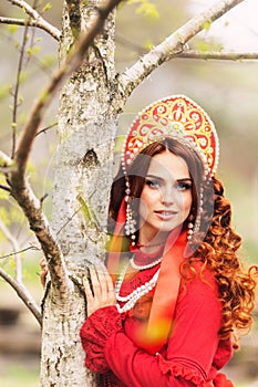 russian girl in traditional russian sarafan and kokoshnik embroidering outdoors