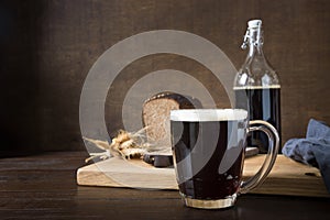 Russian kvass from rye bread in special half-liter mug with loaf bread on dark. Fermented beverage