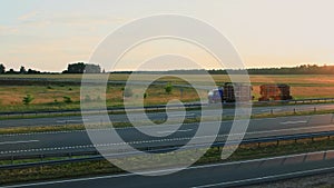 Russian logging trucks, two timber lorry hauling forest logs on semi-trailer on countryside highway at sunset