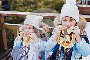 Russian national festival Maslenitsa, shrovetide. Little cute beautiful European girls in headscarf eat big tasty pancakes and