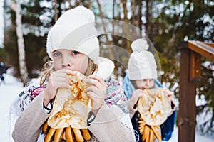 Russian national festival Maslenitsa, shrovetide. Little cute beautiful girls in headscarf eat big tasty pancakes, have