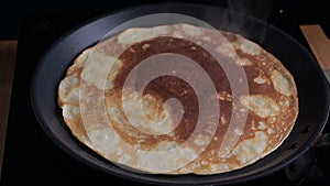 Russian pancake is fried in a pan. The process of making thin pancakes for carnival.