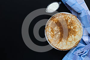 Russian pancakes and sour cream with checker napkin on black background.