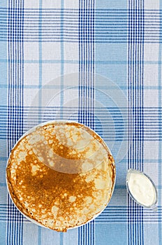 Russian pancakes with sour cream on checker tablecloth