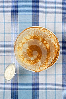 Russian pancakes with sour cream on checker tablecloth