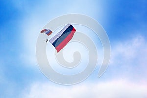 Russian paratrooper jumps with a parachute painted in the colors of the flag of Russia with the Russian flag on clear blue sky