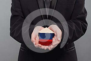 Russian person holding wooden house with flag of Russia. Finance, investment, mortgage, loan and credit concept