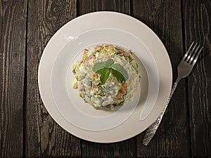 Russian salad Olivier with pickled cucumbers and green peas, boiled potatoes, carrots and eggs with white sauce and ham on a plate