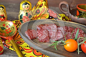 Russian salami sausages sliced on rustic wooden plate, bright matroshka dolls, spoon khokhloma photo