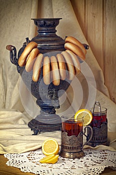 Russian samovar, tea with lemon in faceted glasses with cup holders and bublik. Tinted photo in vintage style