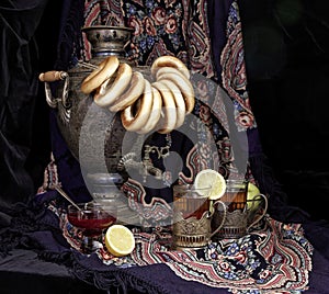 Russian samovar, tea with lemon in faceted glasses with cup holders and bublik. Tinted photo in vintage style on black background