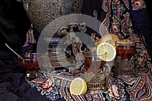 Russian samovar, tea with lemon in faceted glasses with cup holders and bublik. Tinted photo in vintage style on black background