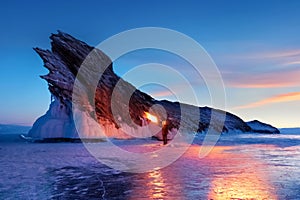 Russian Siberian fiery landscape. Sunrise at Lake Baikal. Silhouette of a man with a torch on the background of a rock.