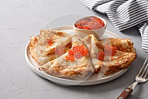 Russian thin pancakes or blini with red caviar on grey.