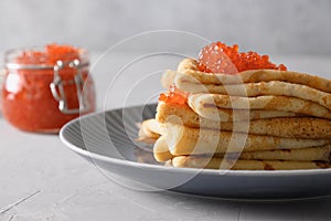 Russian thin pancakes with red caviar on grey table.