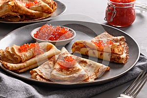 Russian thin pancakes with red caviar on grey table.