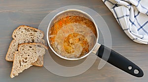 Russian traditional food. Vegetable soup shchi in a ladle and bread on a gray background. Top view