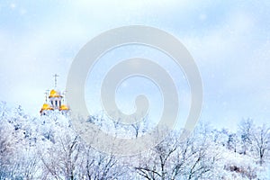 Russian winter landscape. Golden domes of the church against the background of a winter white forest. Snowing.