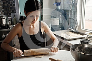 Russian woman beatifull brunette kneading bread dough with rolling pin on kitchen table.