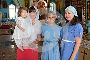 Russian women before toddler baptism are in church, godmother with goddaughter, mother with teenager daughter, indoor portrait