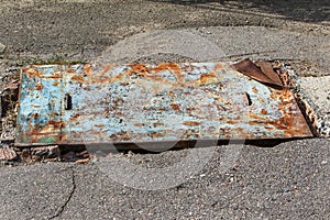 Rust background. A piece of old rusty metal lies on the road and closes a large hole in the old cracked asphalt. Bad paved road