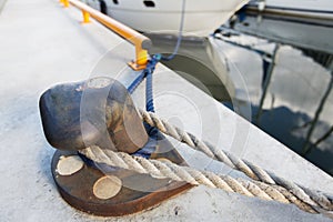 Rusted iron mooring bollard with rope on pier