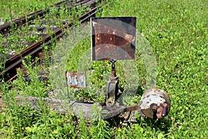 Rusted metal black and white railway switch mechanism with metal sign mounted on wooden board