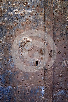 A rusted metal door with three rings, and an antique lock