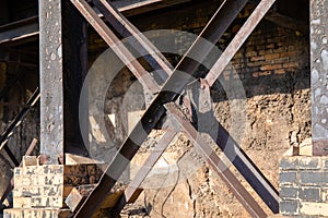 Rusted metal girders in front of an old brick wall, sunshine and shadows