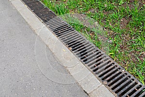 A rusted metal sewer grate along a paved walkway. The edge of the pavement