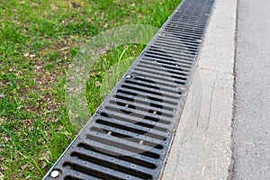 A rusted metal sewer grate along a paved walkway. The edge of the pavement.