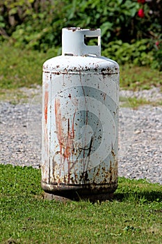 Rusted old light grey propane tank or grill cylinder used for powering barbeque grill left outside of family house