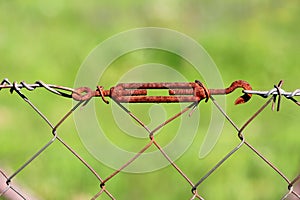 Rusted old vintage wire fence grey metal tensioner closeup on light green background