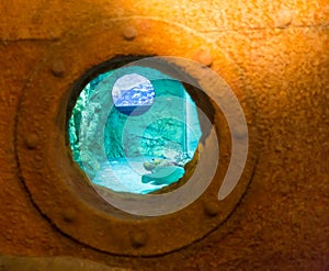 Rusted streaked round porthole in the side of an old white painted ship with blue surface at the bottom