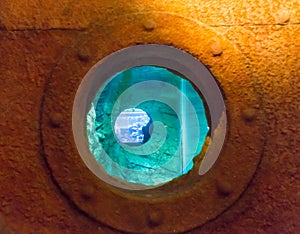 Rusted streaked round porthole in the side of an old white painted ship with blue surface at the bottom