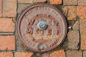 Rusted water meter access hatch on a brick street