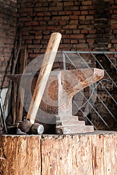 Rustic anvil and hammer on wooden stump.