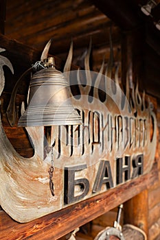 Rustic bell hanging from wooden structure with Banya sign in Cyrillic letters