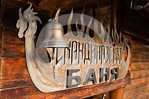 Rustic bell hanging from wooden structure with Banya sign in Cyrillic letters