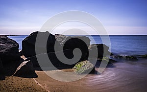 Rustic black boulders on the beach on Cape Cod, long exposure photo