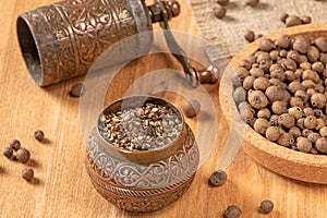 Rustic black pepper mill and whole peppercorns on wooden background